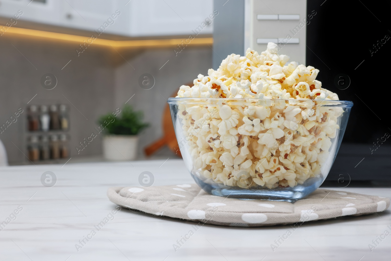 Photo of Tasty popcorn in bowl near microwave oven on white marble table indoors, space for text