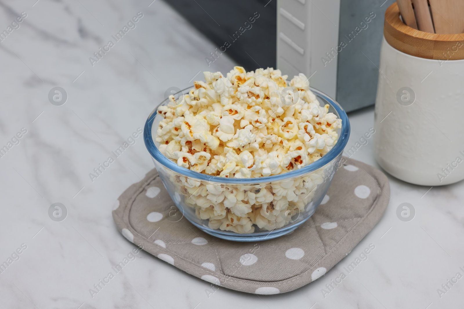 Photo of Tasty popcorn in bowl near microwave oven on white marble table, closeup