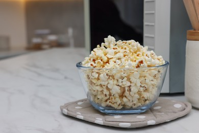 Photo of Tasty popcorn in bowl near microwave oven on white marble table indoors, space for text