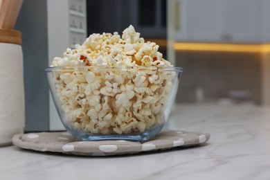 Photo of Tasty popcorn in bowl near microwave oven on white marble table indoors, space for text