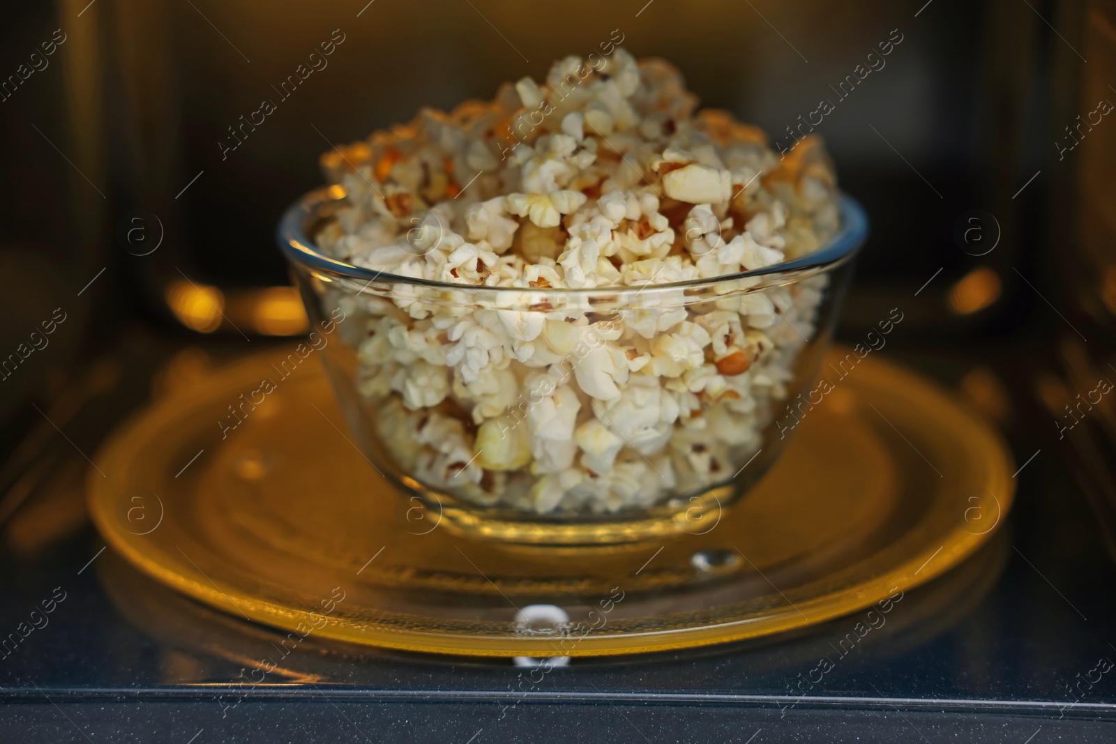 Photo of Bowl of tasty popcorn in microwave oven, closeup