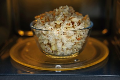 Photo of Bowl of tasty popcorn in microwave oven, closeup