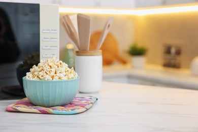 Photo of Tasty popcorn in bowl near microwave oven on light marble table indoors, space for text