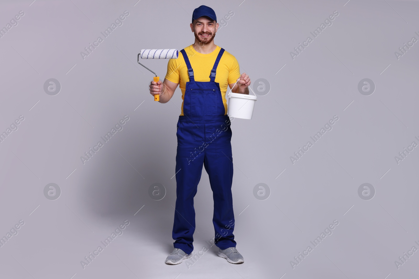 Photo of Professional painter with roller and bucket of paint on light grey background