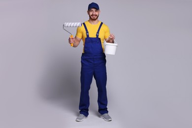 Professional painter with roller and bucket of paint on light grey background