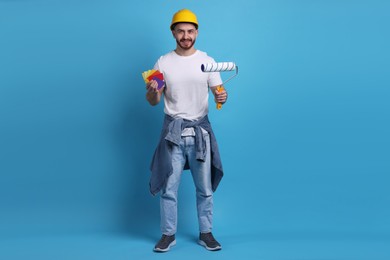 Photo of Man wearing hardhat with roller and color samples on blue background