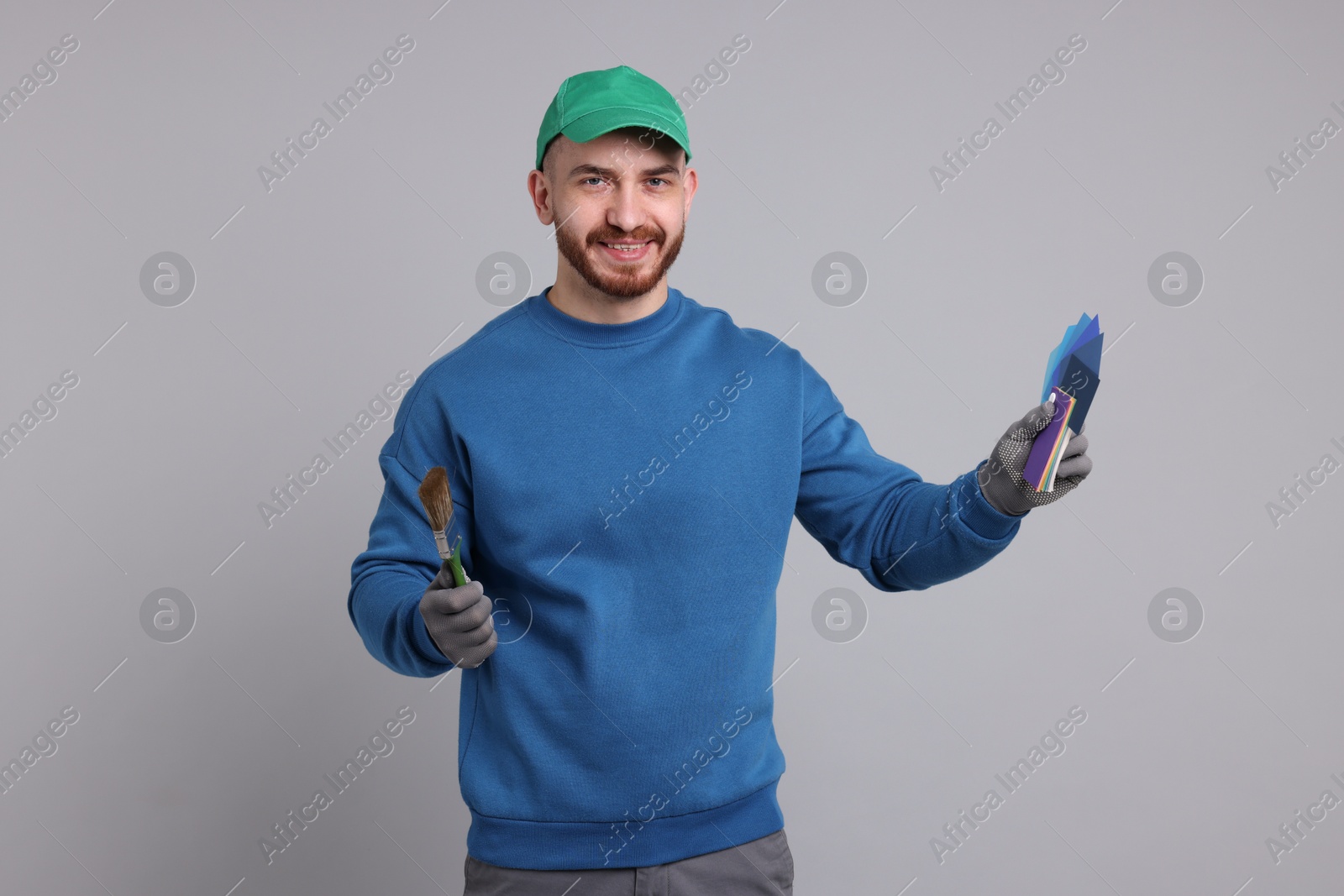 Photo of Man with paintbrush and color samples on light grey background