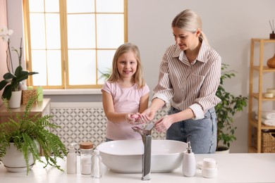 Happy mother and daughter washing their hands in bathroom