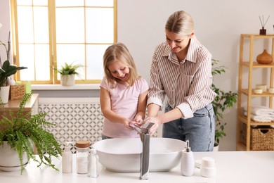 Happy mother and daughter washing their hands in bathroom