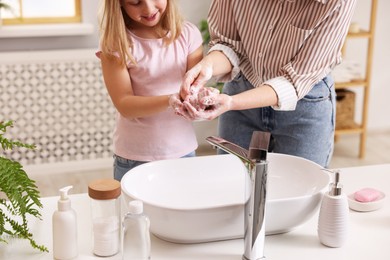 Mother and daughter washing their hands indoors, closeup