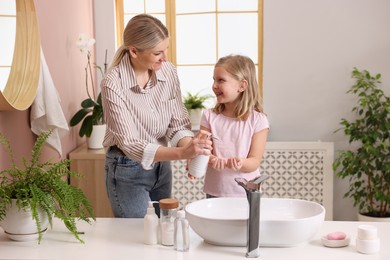 Happy mother and daughter washing their hands in bathroom