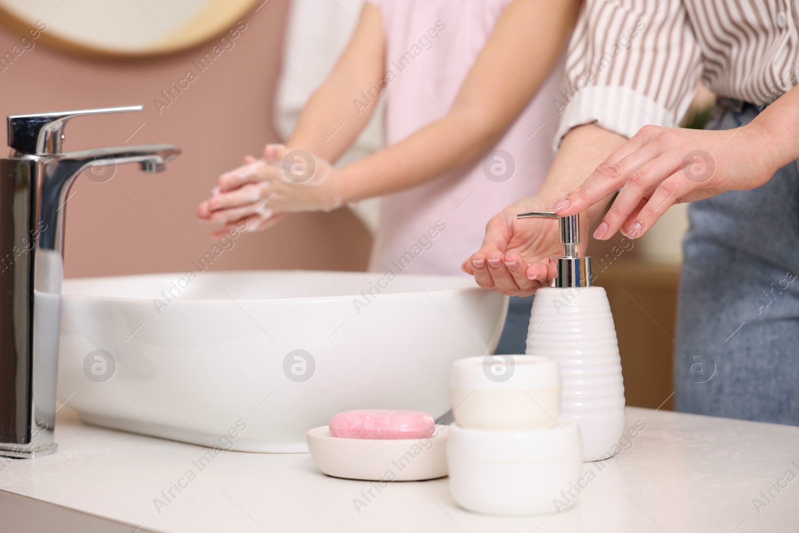 Photo of Mother and daughter washing their hands indoors, closeup