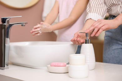 Mother and daughter washing their hands indoors, closeup