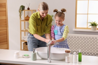 Happy mother and daughter washing their hands in bathroom