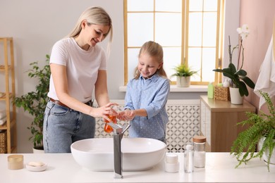 Happy mother and daughter washing their hands in bathroom