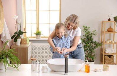 Happy mother and daughter washing their hands in bathroom