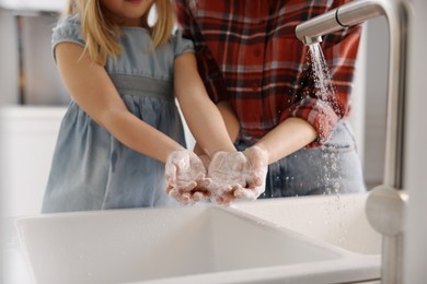 Photo of Mother and daughter washing their hands above sink indoors, closeup