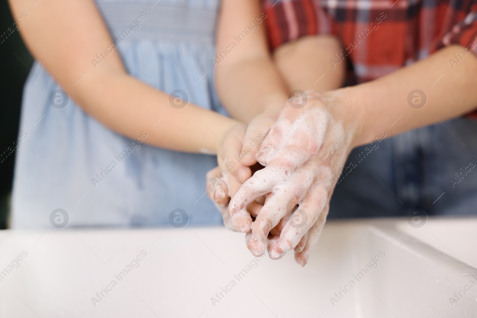 Photo of Mother and daughter washing their hands above sink, closeup