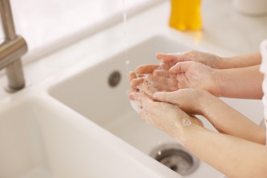 Photo of Mother and daughter washing their hands indoors, closeup. Space for text