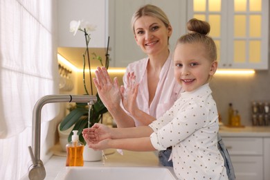 Photo of Happy mother and daughter washing their hands in kitchen