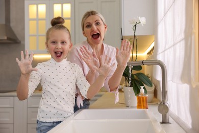 Happy mother and daughter washing their hands in kitchen