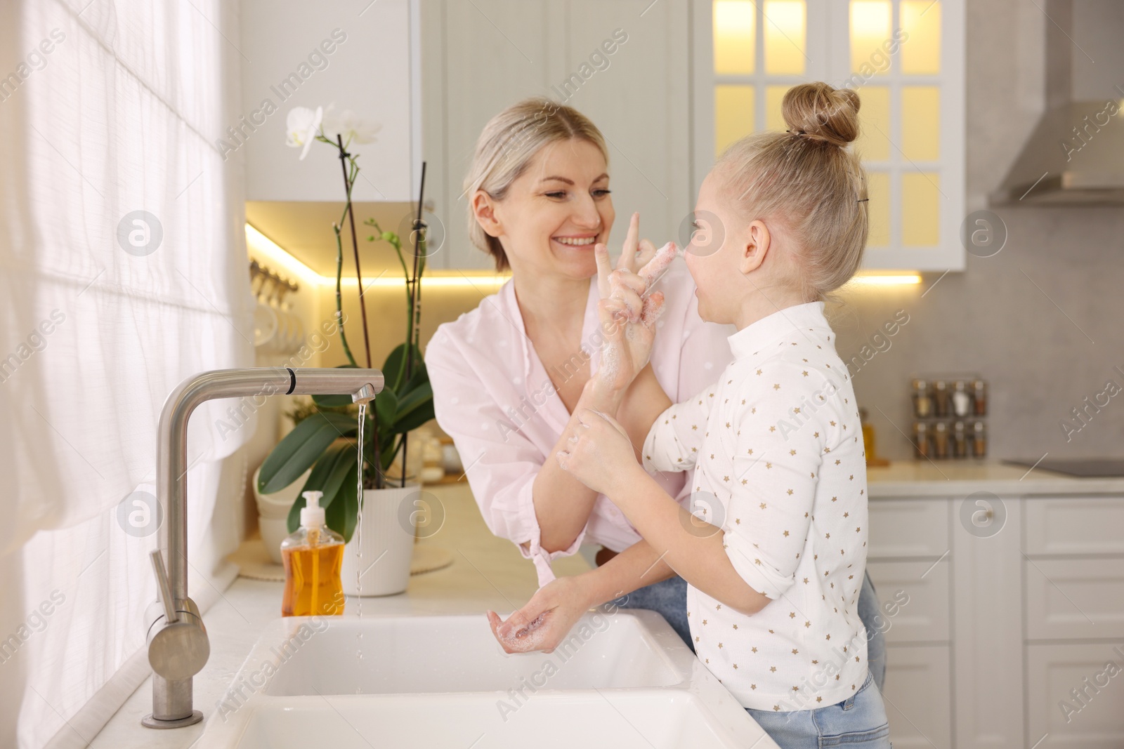 Photo of Happy mother and daughter washing their hands in kitchen