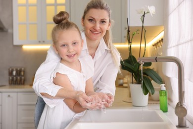 Happy mother and daughter washing their hands in kitchen