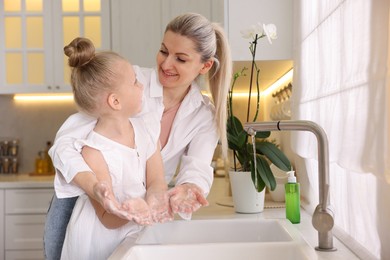 Happy mother and daughter washing their hands in kitchen