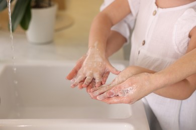 Mother and daughter washing their hands indoors, closeup. Space for text