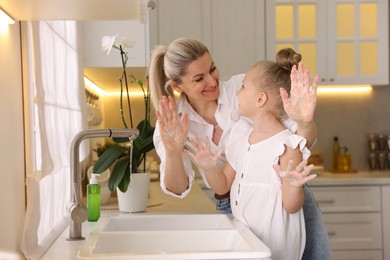 Happy mother and daughter washing their hands in kitchen