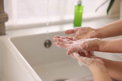 Photo of Mother and daughter washing their hands indoors, closeup