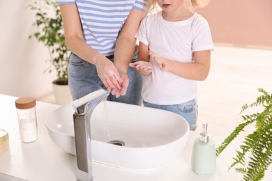 Mother and daughter washing their hands indoors, closeup