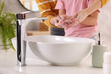 Mother and daughter washing their hands above sink indoors, closeup