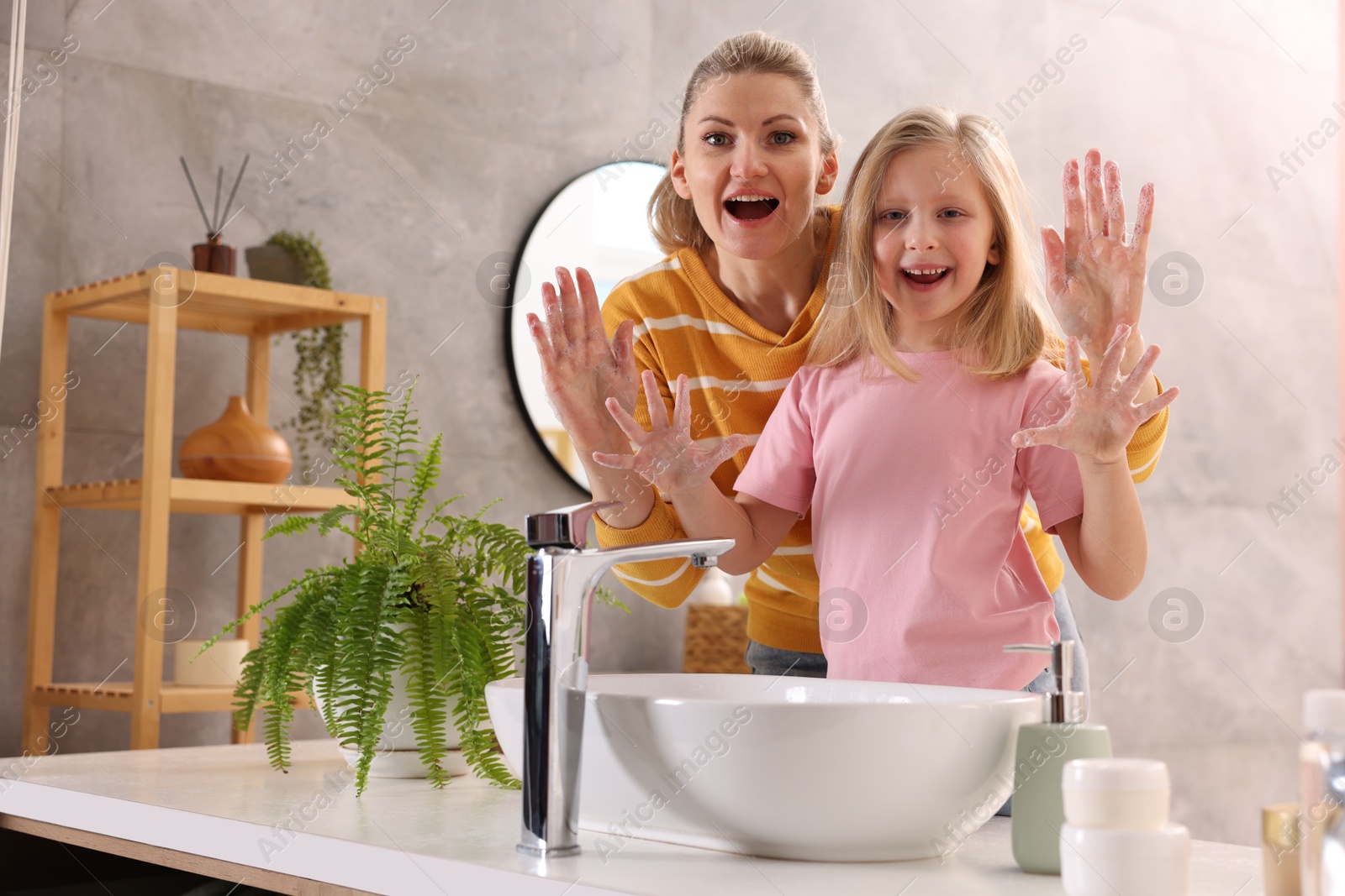 Photo of Happy mother and daughter washing their hands in bathroom