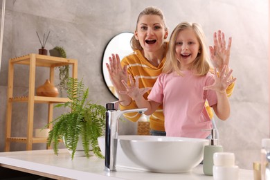 Happy mother and daughter washing their hands in bathroom