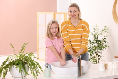 Photo of Happy mother and daughter washing their hands at home