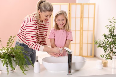 Happy mother and daughter washing their hands at home