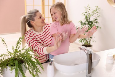 Photo of Happy mother and daughter washing their hands at home