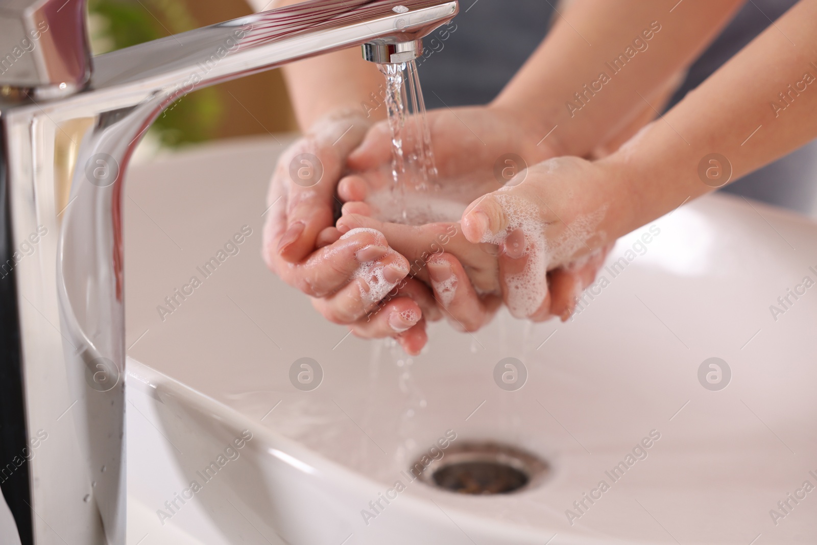 Photo of Mother and daughter washing their hands above sink indoors, closeup