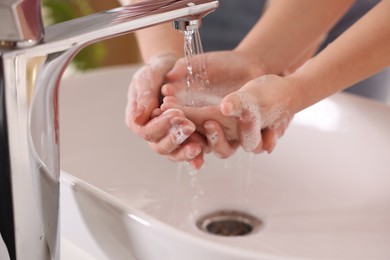 Photo of Mother and daughter washing their hands above sink indoors, closeup