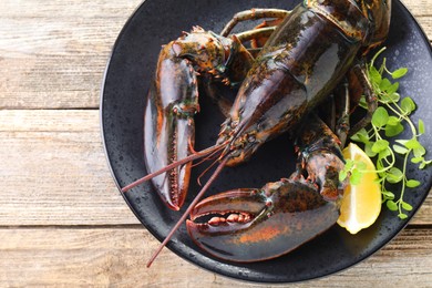 Photo of Raw lobster, piece of lemon and microgreens on wooden table, top view