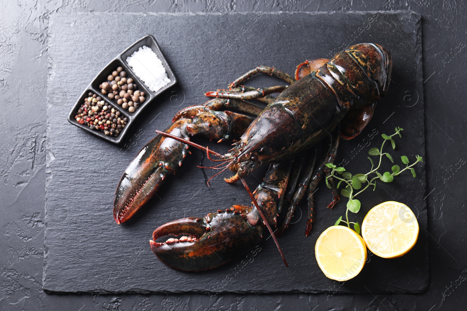 Photo of Raw lobster, cut lemon, microgreens and spices on dark textured table, top view