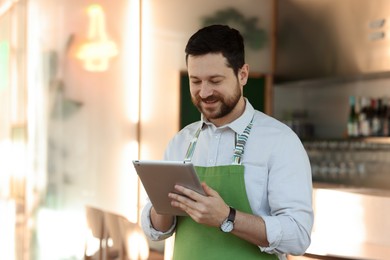 Smiling business owner working with tablet in his cafe. Space for text