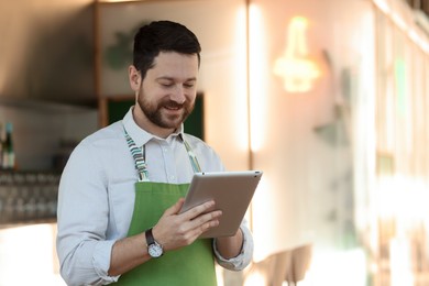 Photo of Smiling business owner working with tablet in his cafe. Space for text