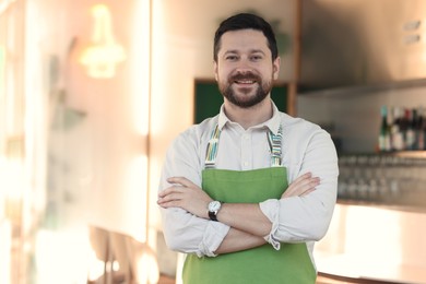 Photo of Portrait of smiling business owner with crossed arms in his cafe. Space for text