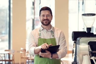 Photo of Smiling business owner working with clipboard in his cafe