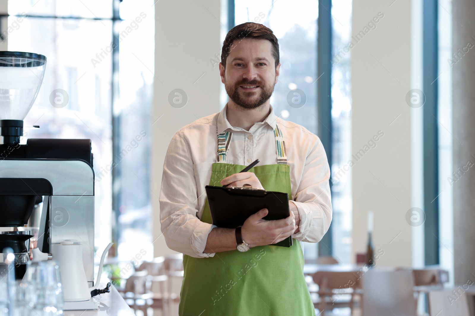 Photo of Smiling business owner working with clipboard in his cafe