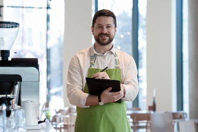 Photo of Smiling business owner working with clipboard in his cafe