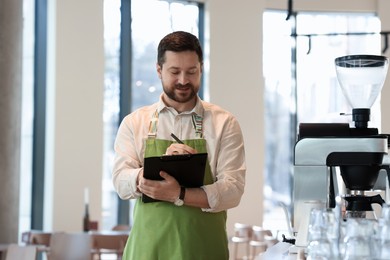 Photo of Handsome business owner working with clipboard in his cafe