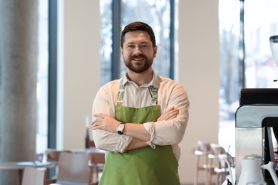 Photo of Portrait of smiling business owner with crossed arms in his cafe